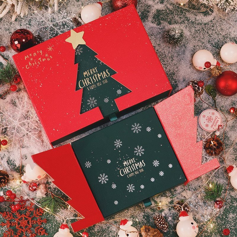 Christmas themed cardboard gift boxes surrounded by ornaments and snowmen on snowy ground