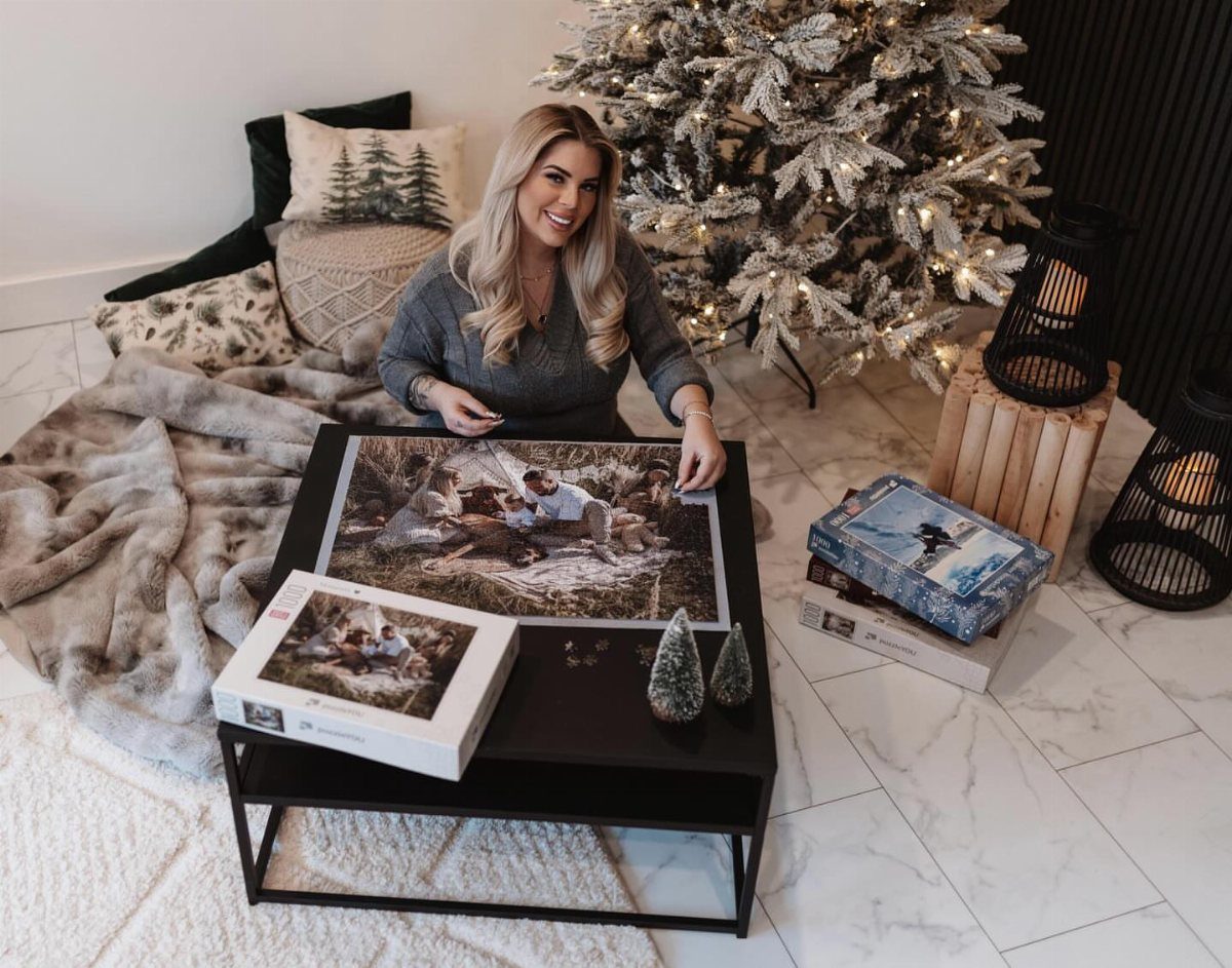 Woman sitting by a Christmas tree with a completed custom photo puzzle on a table