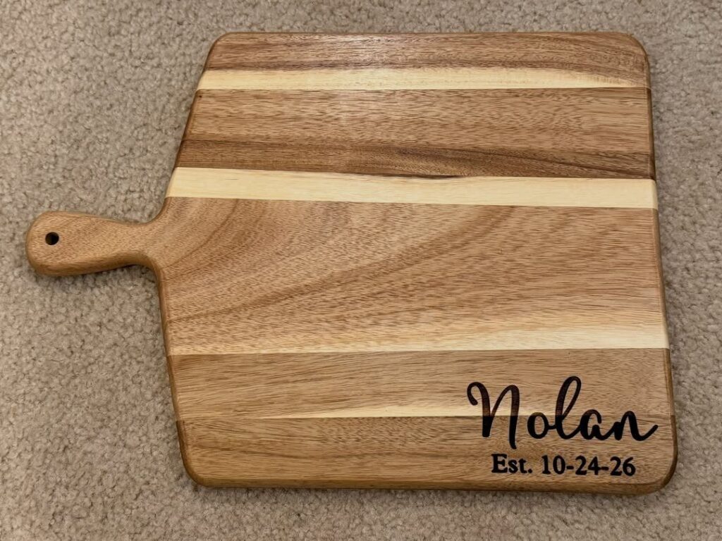 Wooden cutting board with engraved name Nolan and date on beige carpet