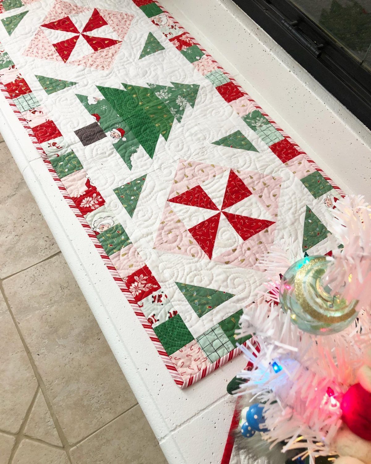 Christmas quilted table runner with tree and pinwheel patterns on a white surface