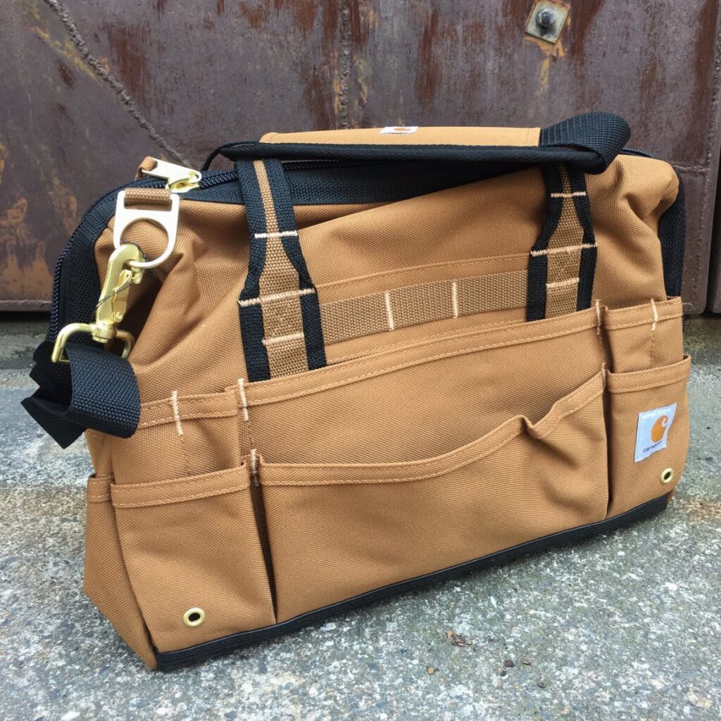Brown Carhartt canvas tool bag with black straps on a concrete surface.