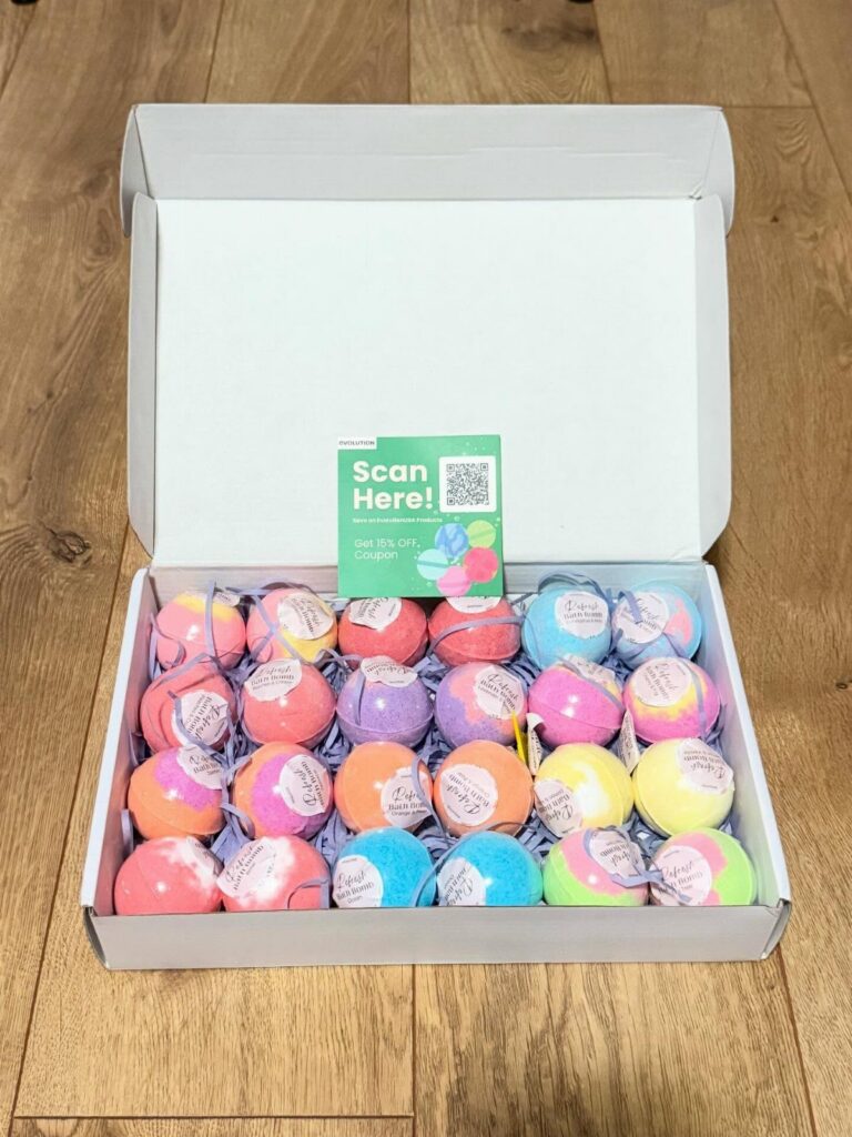 Colorful spherical bath bombs arranged in a white cardboard box on wooden flooring.