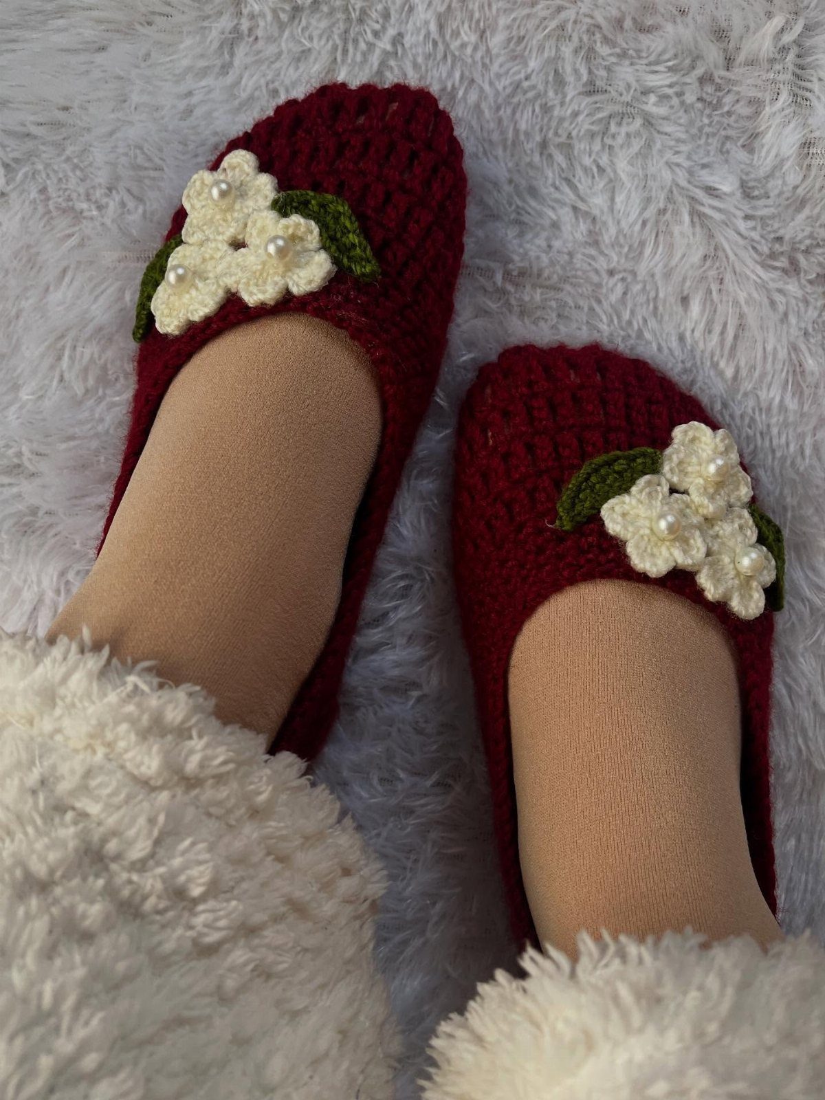 Burgundy crochet slipper socks with white flower accents on a white fluffy rug