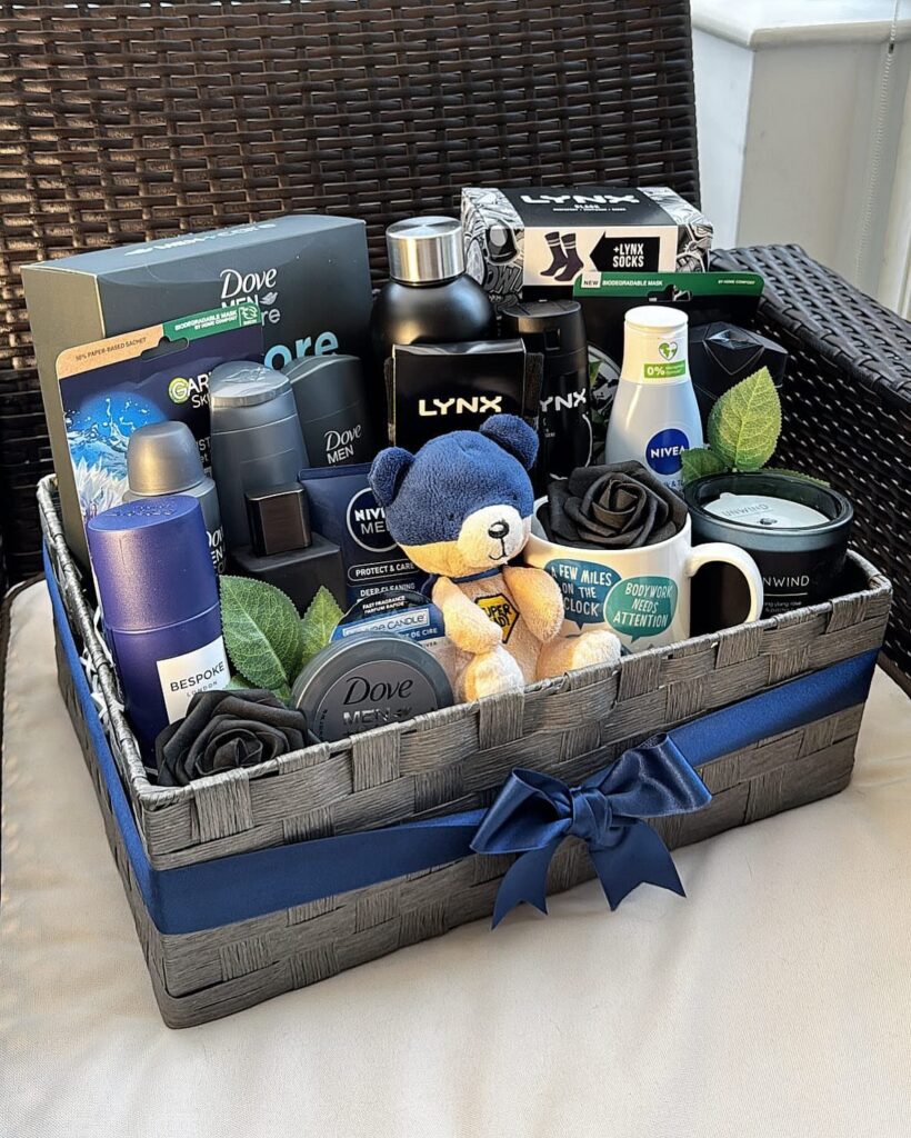 Grey woven gift basket filled with men's toiletries, a blue teddy bear, and a mug.