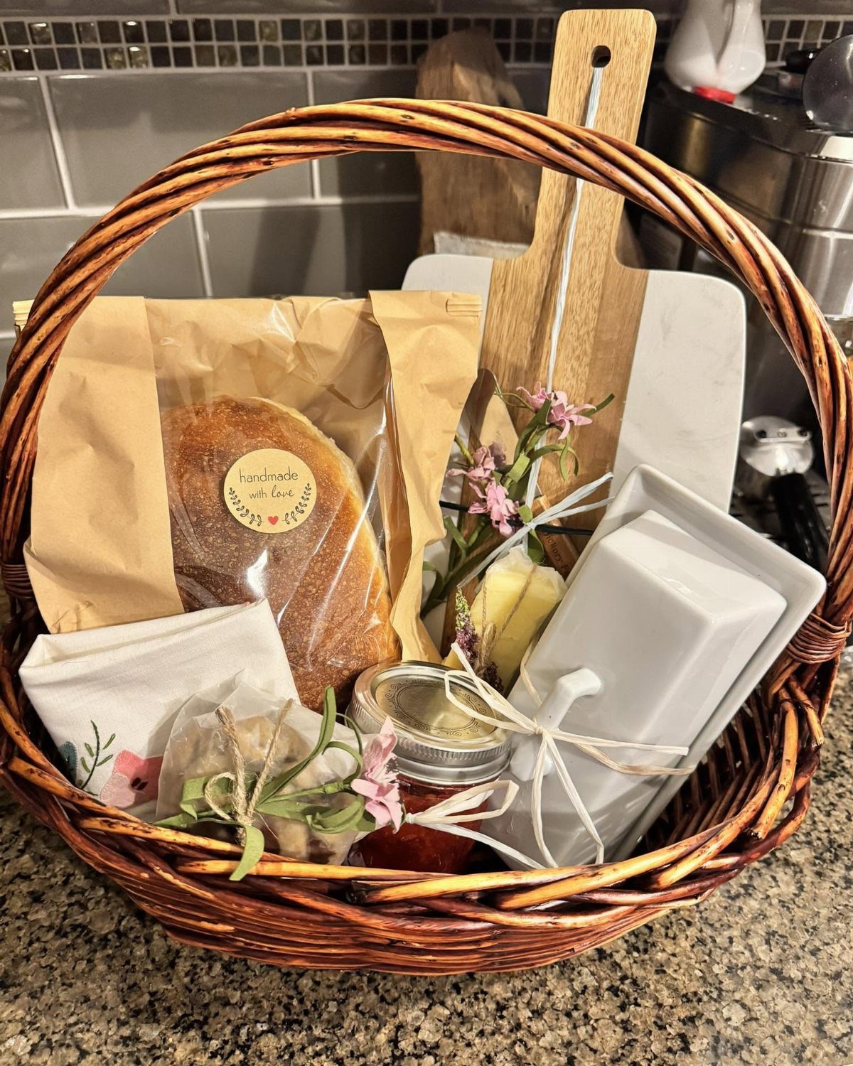Wicker gift basket with homemade bread, jam, and a white ceramic butter dish.