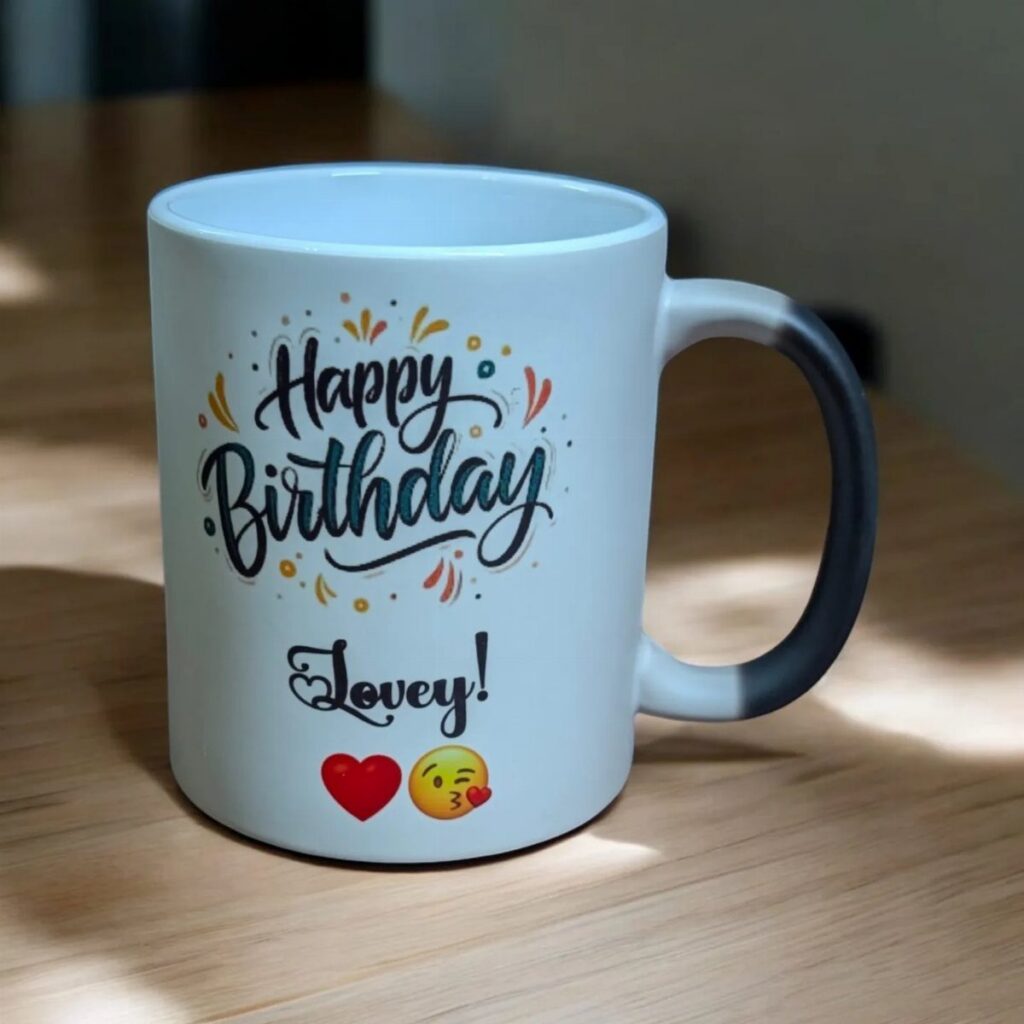 White ceramic mug with Happy Birthday Lovey text and emojis on wooden table