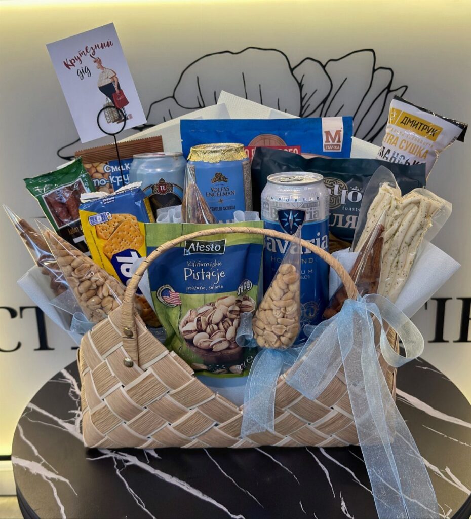 Woven gift basket filled with beer, pistachios, and snacks on a marble table.