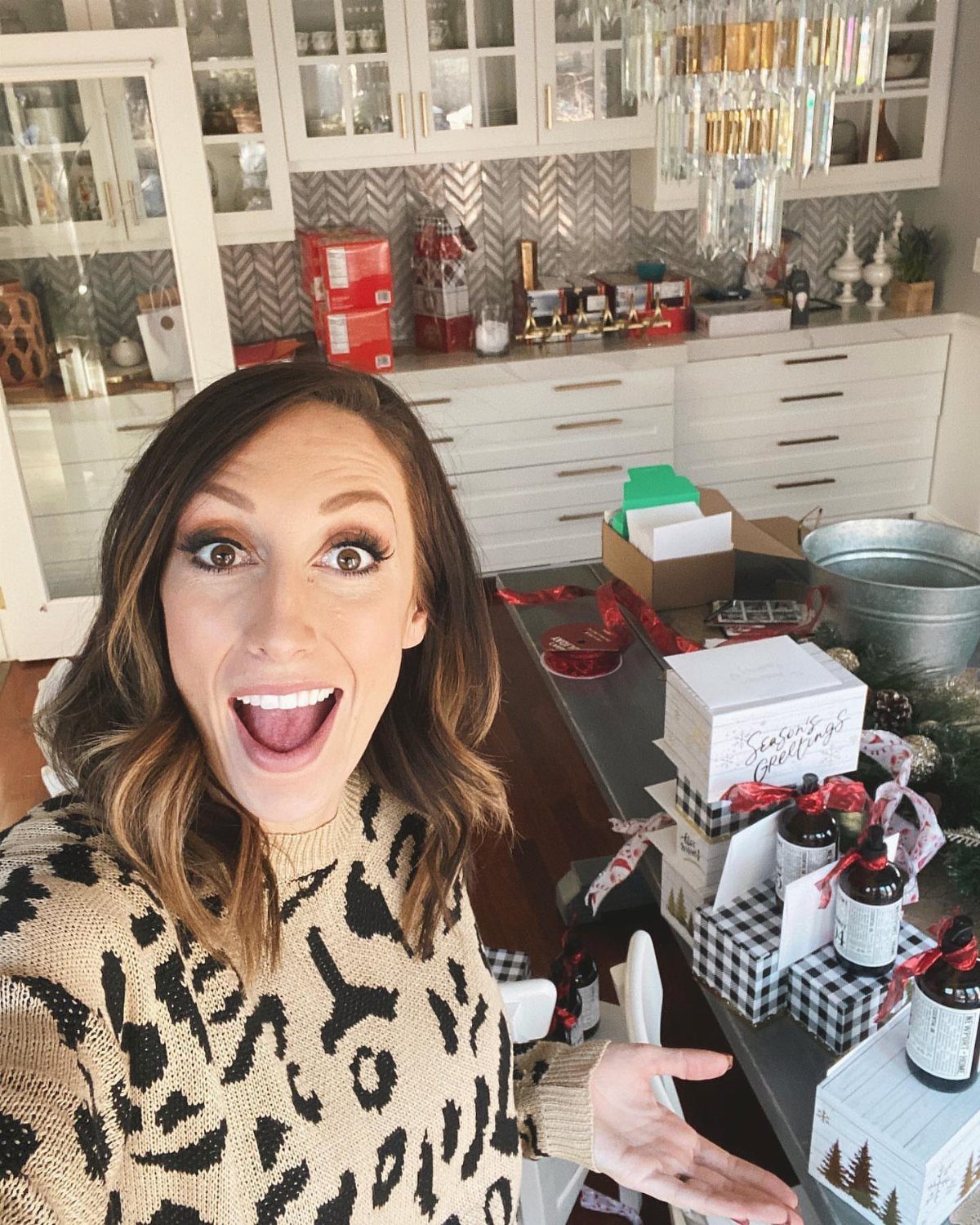 Woman in leopard print sweater posing with wrapped Christmas gift boxes in kitchen