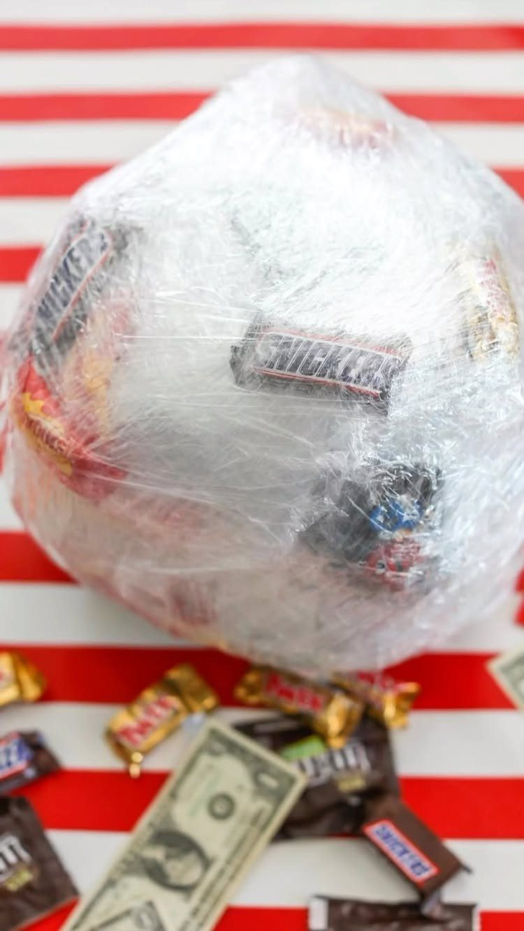 Saran wrap ball filled with candy and money on red striped background