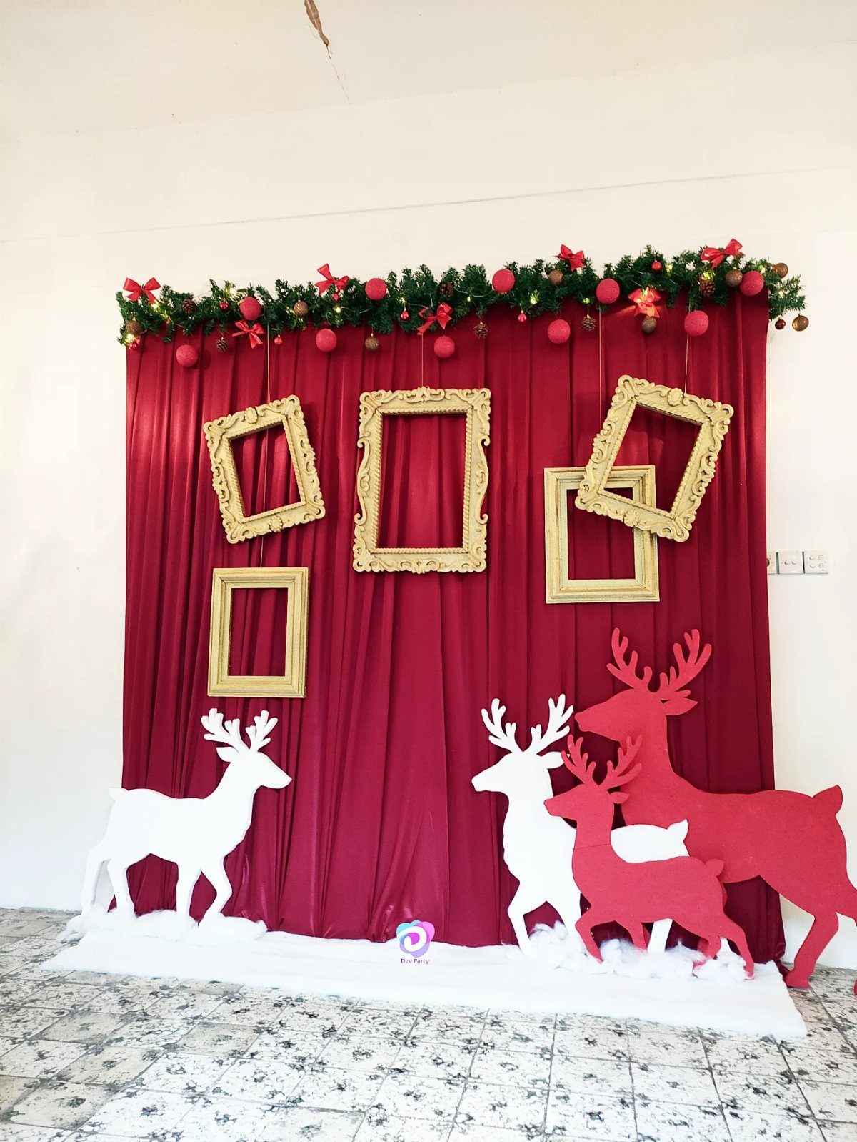 Red curtain backdrop with gold frames and reindeer cutouts for a holiday photo booth
