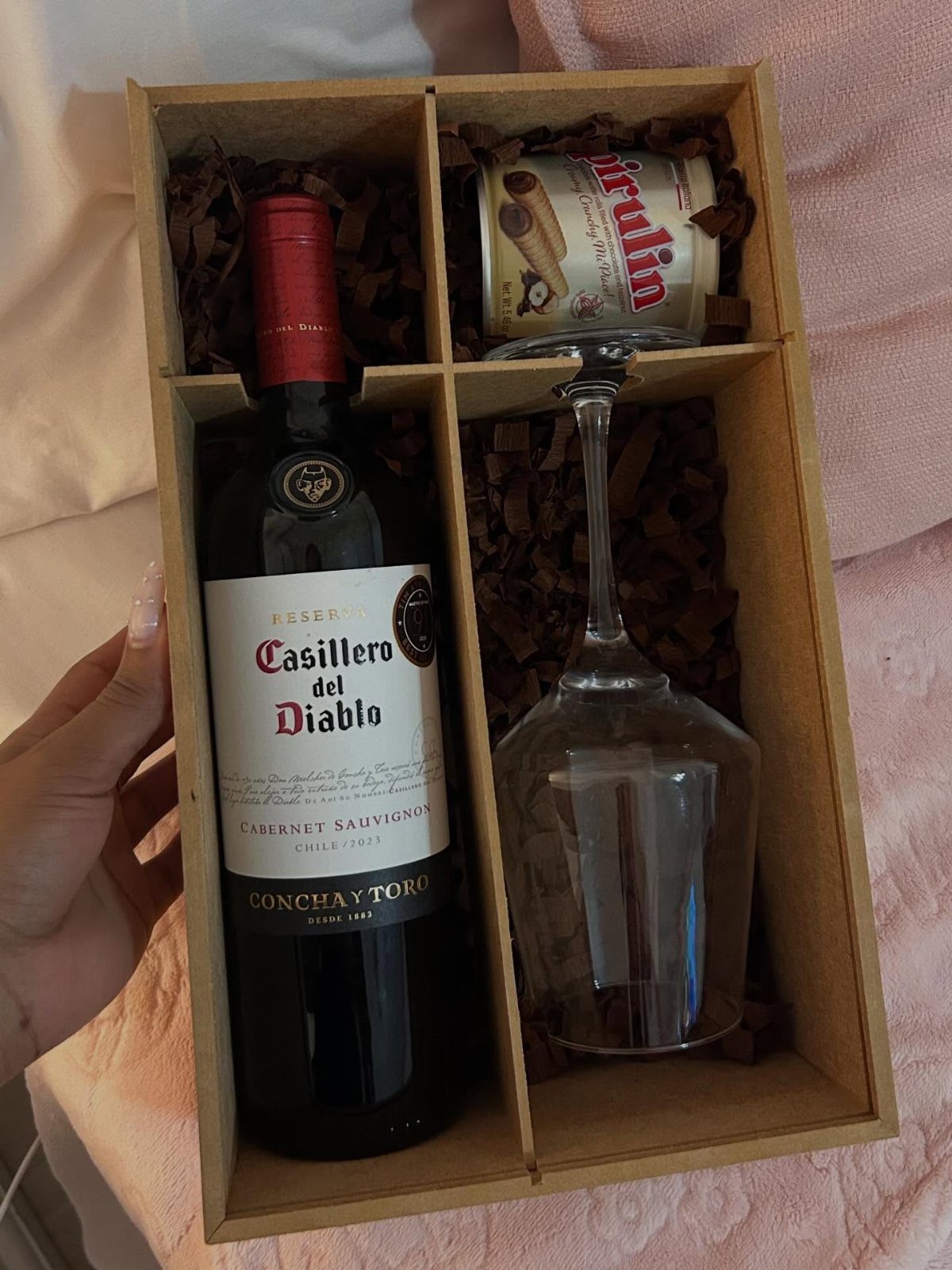 Wine bottle, wine glass, and chocolates arranged in a brown gift box.