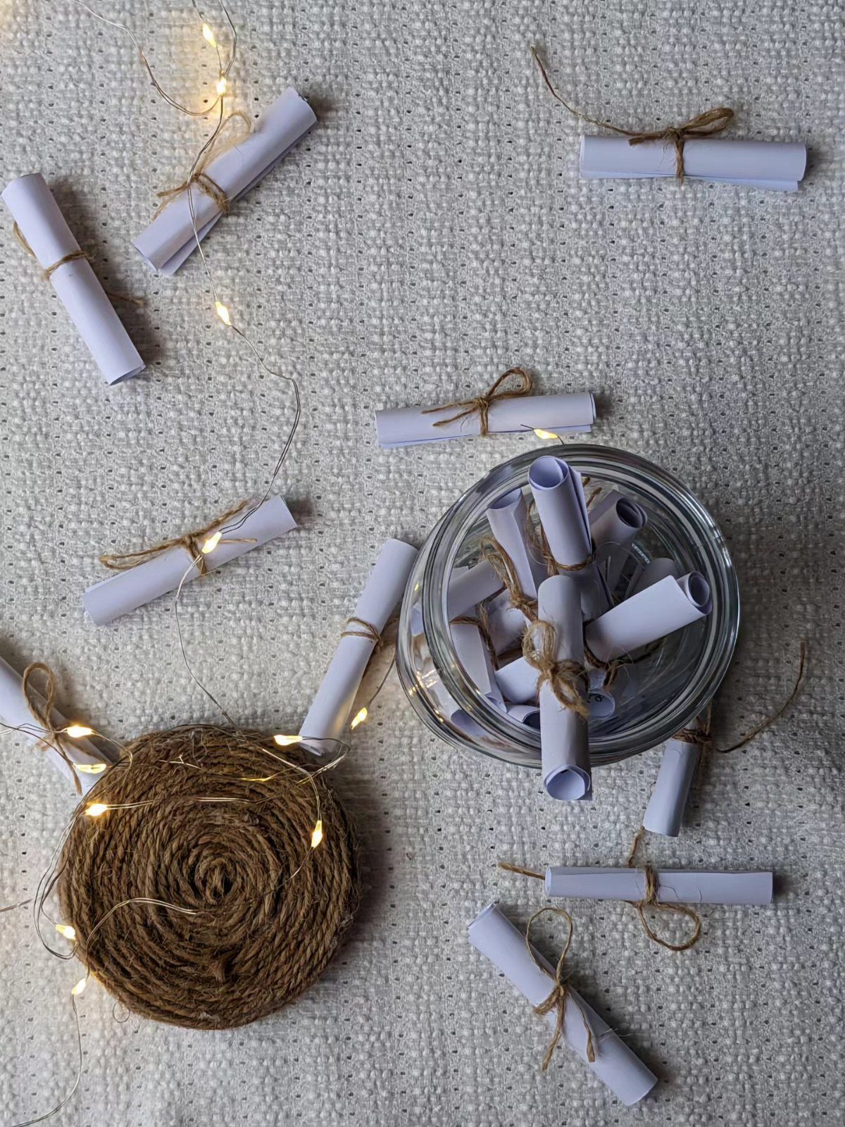 Glass jar filled with small white paper scrolls tied with brown twine.