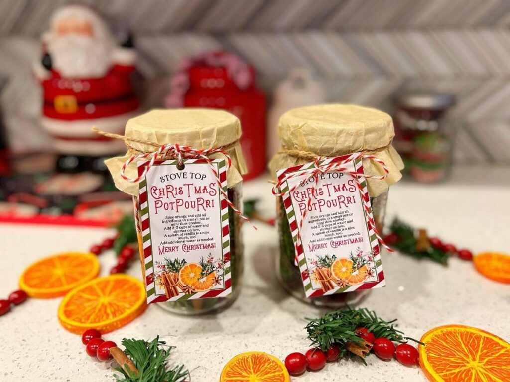 Two mason jar Christmas potpourri gifts with fabric lids and festive labels.