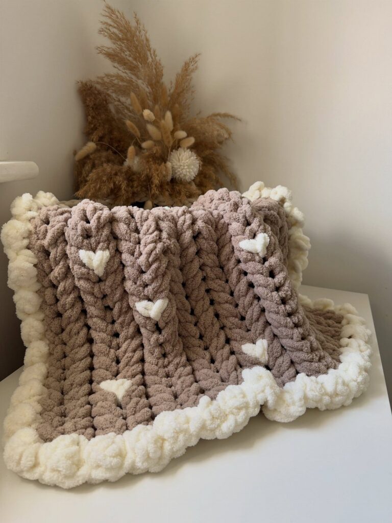 Chunky mauve knitted blanket with white hearts and a fluffy white border.