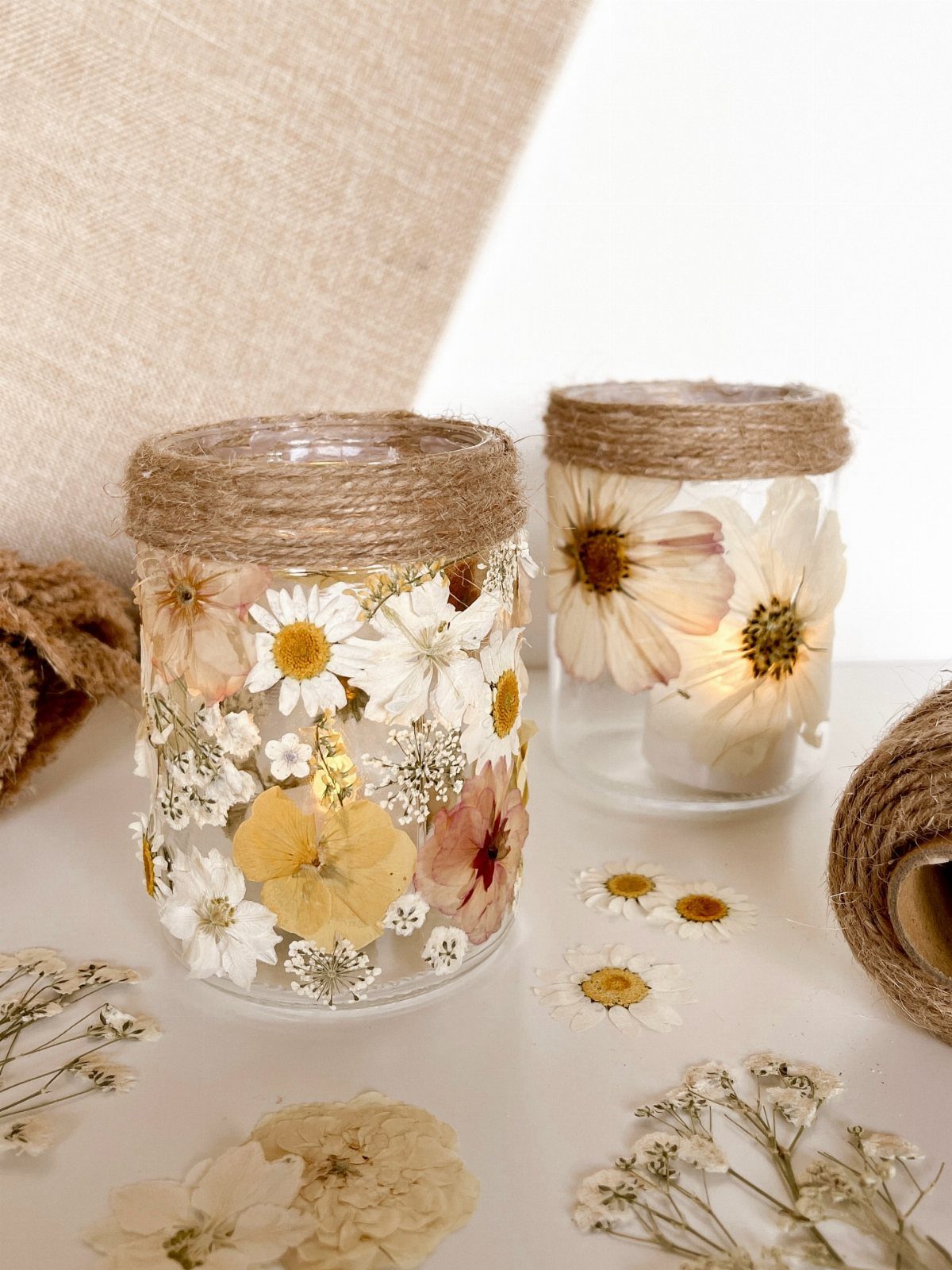 Two mason jar vases decorated with pressed flowers and twine rope rims.