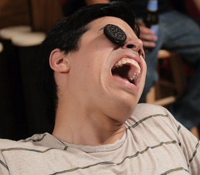 Man tilting head back to eat a cookie resting on his forehead.