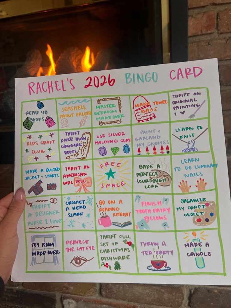 Hand-drawn 2026 Bingo card with colorful goals held in front of a fireplace.
