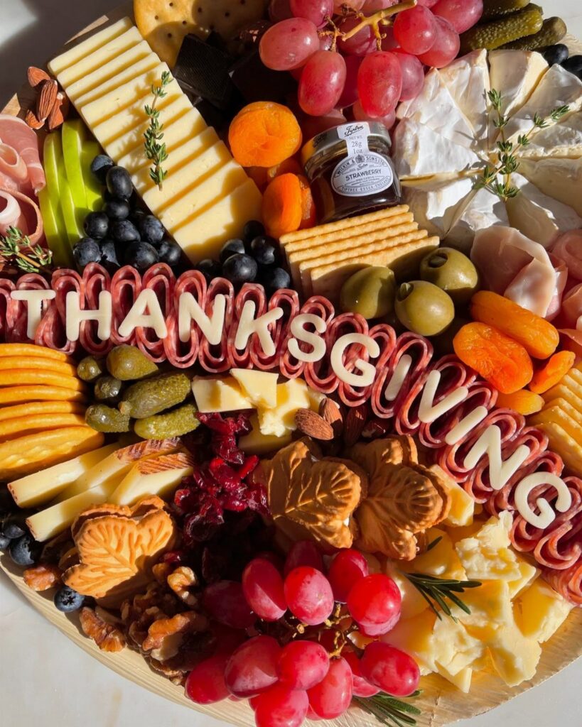 Thanksgiving charcuterie board with assorted cheeses, fruits, meats, and 'THANKSGIVING' letter cutouts.