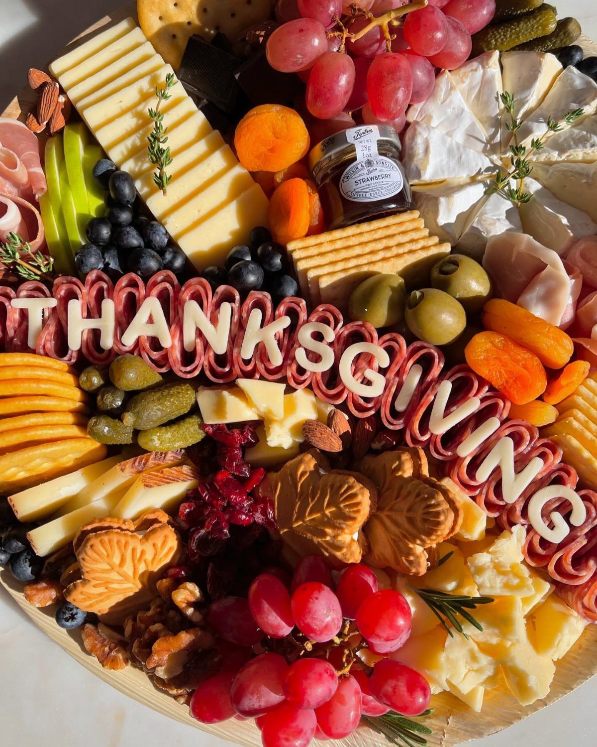 Thanksgiving charcuterie board with assorted cheeses, fruits, meats, and 'THANKSGIVING' letter cutouts.
