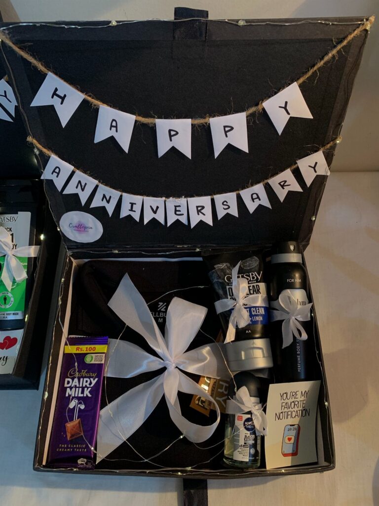 Anniversary gift box for him with black clothing, chocolate, and a celebratory banner.