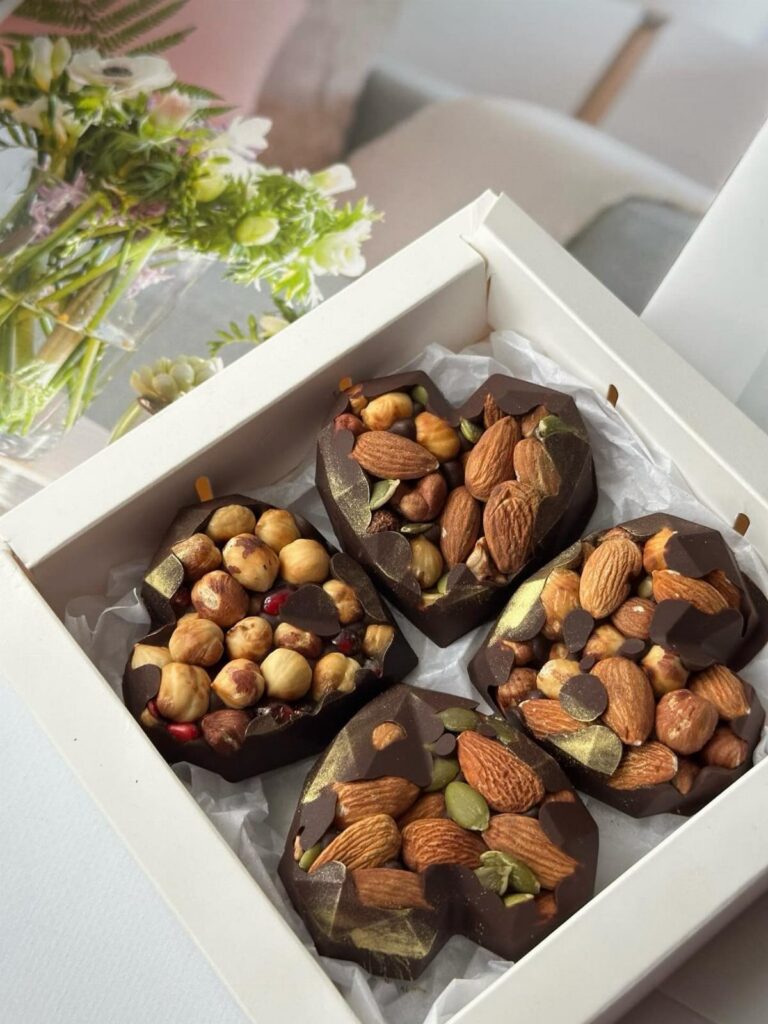 Heart-shaped dark chocolates topped with almonds and hazelnuts in a white gift box.