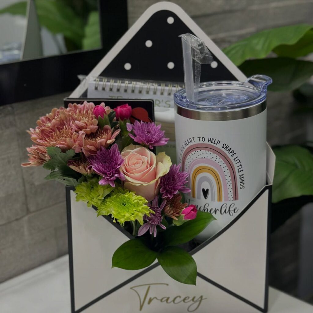 Gift box for a teacher containing flowers, a rainbow tumbler, and a notebook.